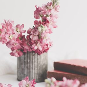 pink flowers on brown wooden vase beside a pile of books -- a sense of happiness