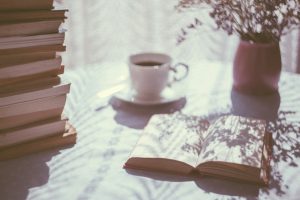 open book beside white ceramic teacup with pile of books on the side