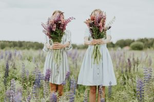 two young girls holding pink petaled flowers on a meadow