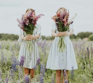 two young girls holding pink petaled flowers on a meadow