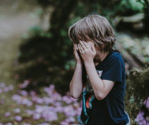 boy covering his face in a forest